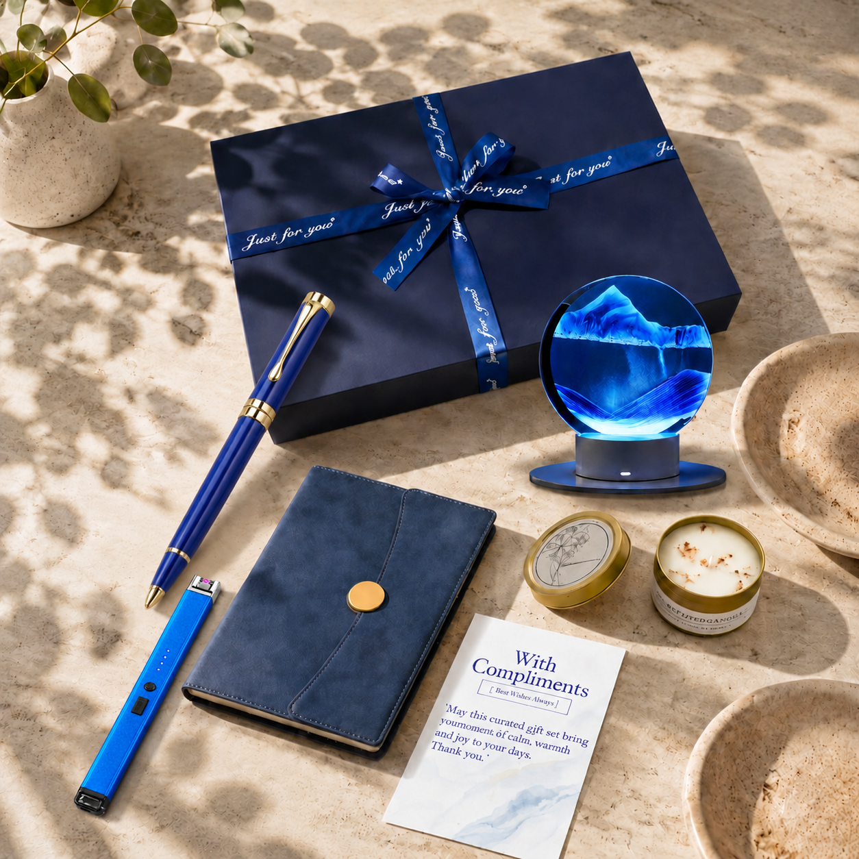 A top-down flatlay view of an open premium navy blue executive gift set, perfectly arranged with a blue leather notebook, a royal blue metal gel pen, and a circular blue moving sand art lamp.