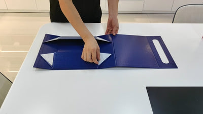 Blue collapsible luxury gift box being assembled from a flat panel